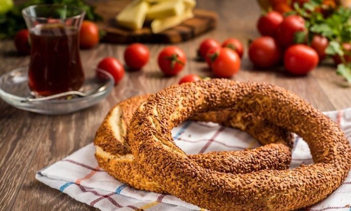 Simit ve Açma Kültürü Şehir Hayatında Değişmeyen Lezzetler Türkiye’de sokak lezzetleri denildiğinde akla gelen ilk tatlar arasında simit ve açma yer alır. Günün her saatinde ulaşılabilen bu iki hamur işi, yalnızca pratik bir atıştırmalık olmanın ötesinde, şehir yaşamının ritmini belirleyen önemli unsurlardan biri olarak görülür. Sabah işe yetişmeye çalışan bir memurun elinde, okul yolunda koşan bir öğrencinin çantasında ya da sahil kenarında çay eşliğinde tüketilen bu lezzetler, toplumsal hafızanın da güçlü bir parçasıdır. Konulu bir haber görseli.